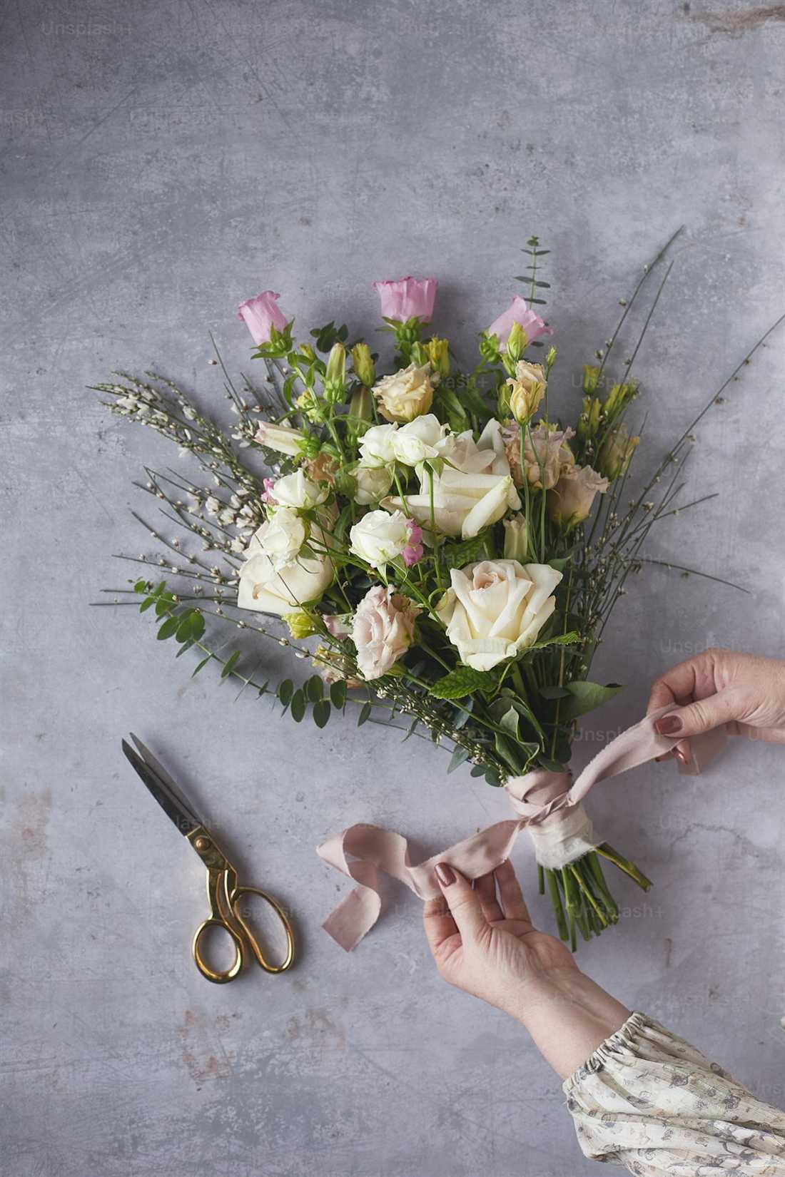 Hands tying a wedding bouquet with dusty rose ribbon